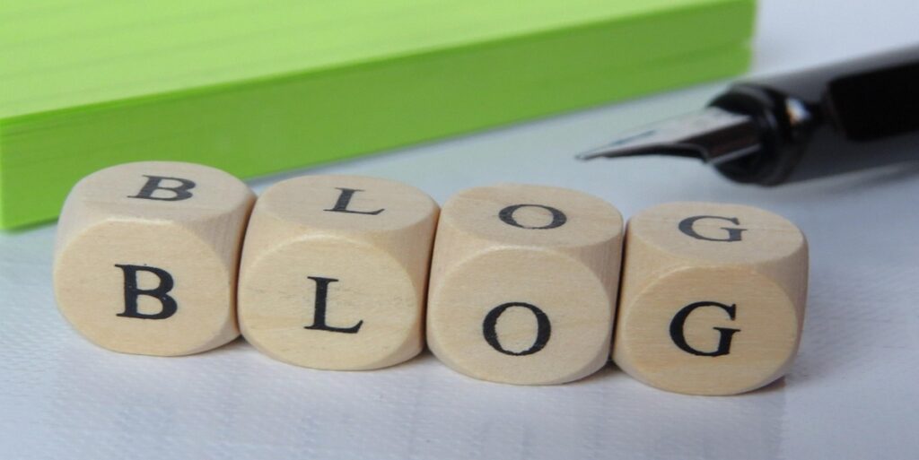ブログ記事作成中のイメージ画像。木製サイコロで「BLOG」の文字、ペン、メモ用紙が写っています