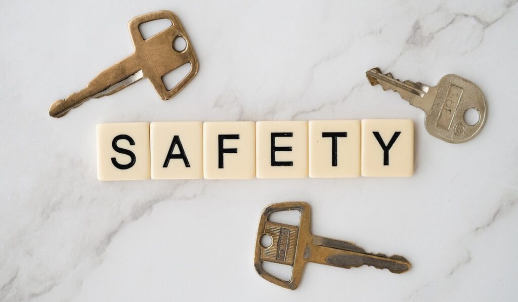 白いタイルに黒字で「SAFETY（安全）」と書かれた文字が並び、その周囲に3つの古風な鍵と1つの現代的な鍵が配置されている。お客様の情報を安全に保護する決意を示す。